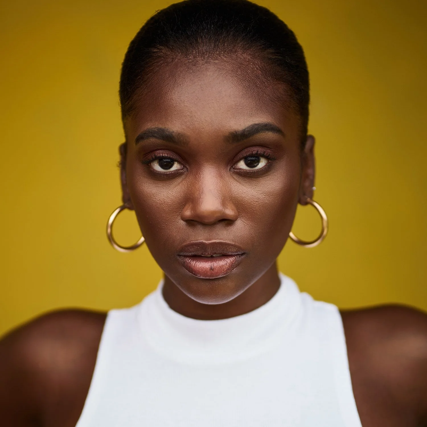 A Black woman looking directly into the camera against a golden background